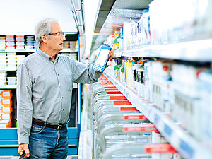 Im Supermarkt: Ein Mann liest prüfend die Beschriftung einer Milchtüte durch. 